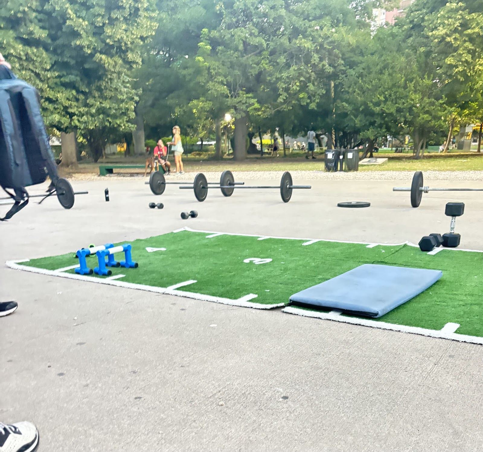 Barras con discos, mancuernas y colchoneta armadas sobre el solado del parque
